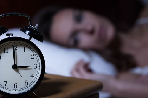 Woman in bed and awake, looking at alarm clock. Sleep and Heart Disease in Women.