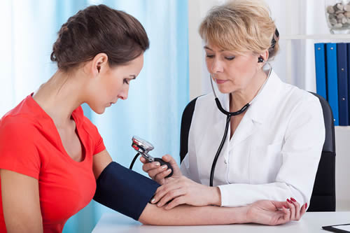 Doctor taking blood pressure of female patient at office.