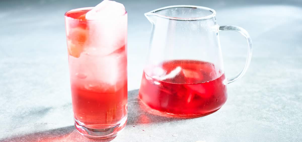 Glass of ginger and hibiscus mocktail next to pitcher.