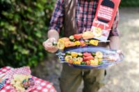Person Holding a Platter of Sliced Fruits and Vegetables on Skewers