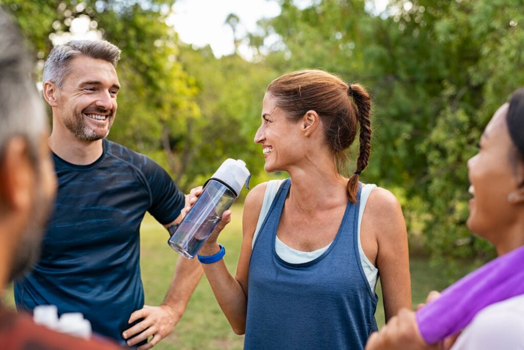 Middle-aged woman drinking water from bottle after fitness exercise.